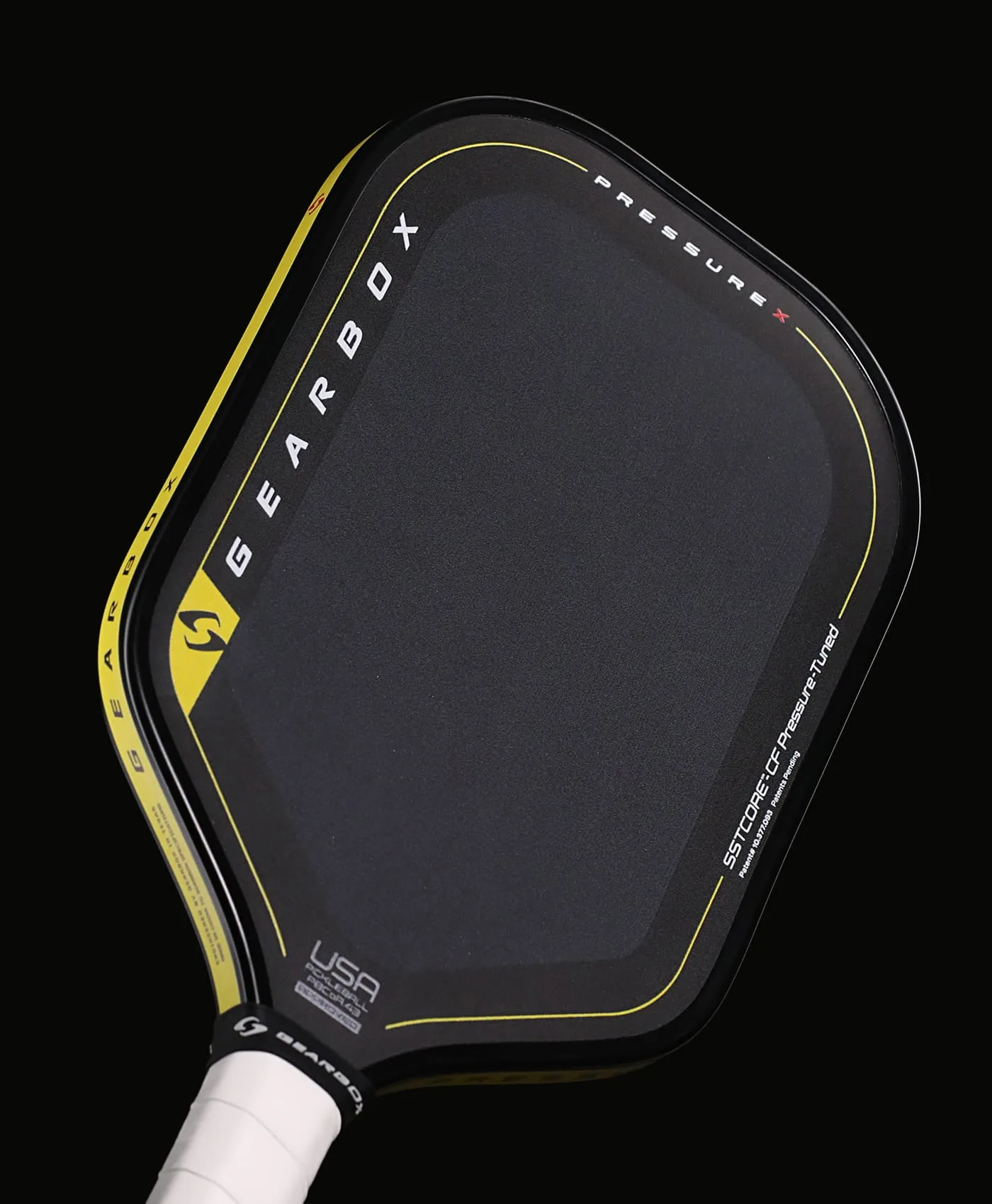 Pressure X 8E đặt nghiêng trên nền tối, mặt carbon đen, viền vàng và logo USA Pickleball gần cổ vợt